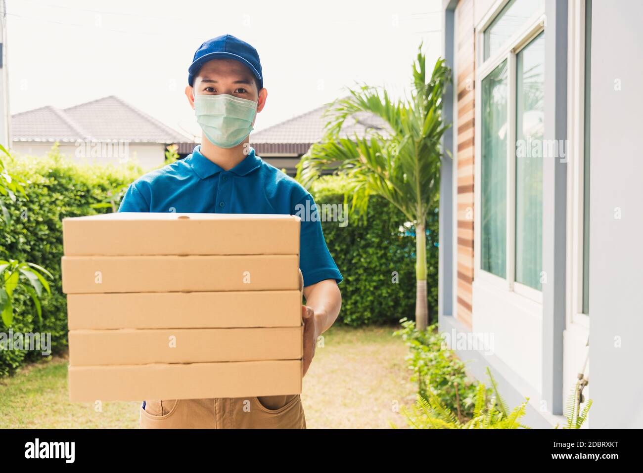 Asiatische junge Lieferung Mann Kurier Senden und Halten Fast Food Pizza in Uniform er schützende Gesichtsmaske Service Kunden zu Hause Tür, unter cur boxed Stockfoto