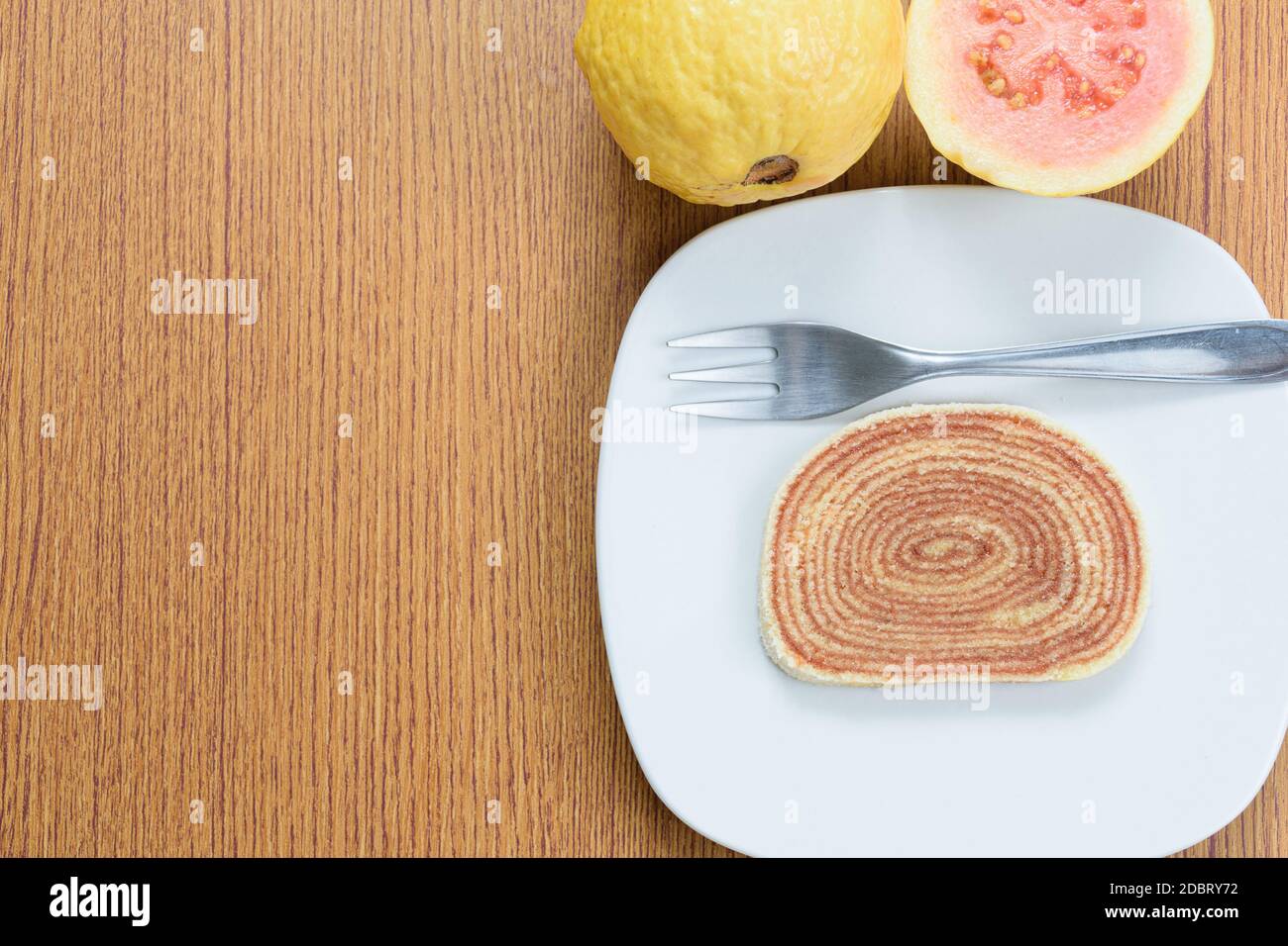 Ein Stück Kuchen (bolo de rolo) neben Guavas und einer Gabel. Stockfoto