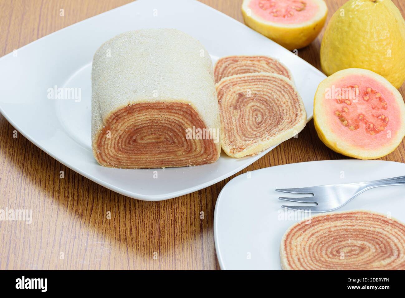 Roll Cake (bolo de rolo) neben Guavas und ein Stück Roll Cake, im Vordergrund verschwommen. Stockfoto