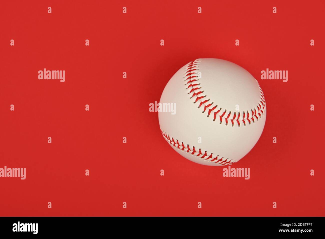 Nahaufnahme eines neuen Baseballballs mit roter Naht auf lebhaftem roten Hintergrund, erhöhte Ansicht von oben, direkt darüber Stockfoto