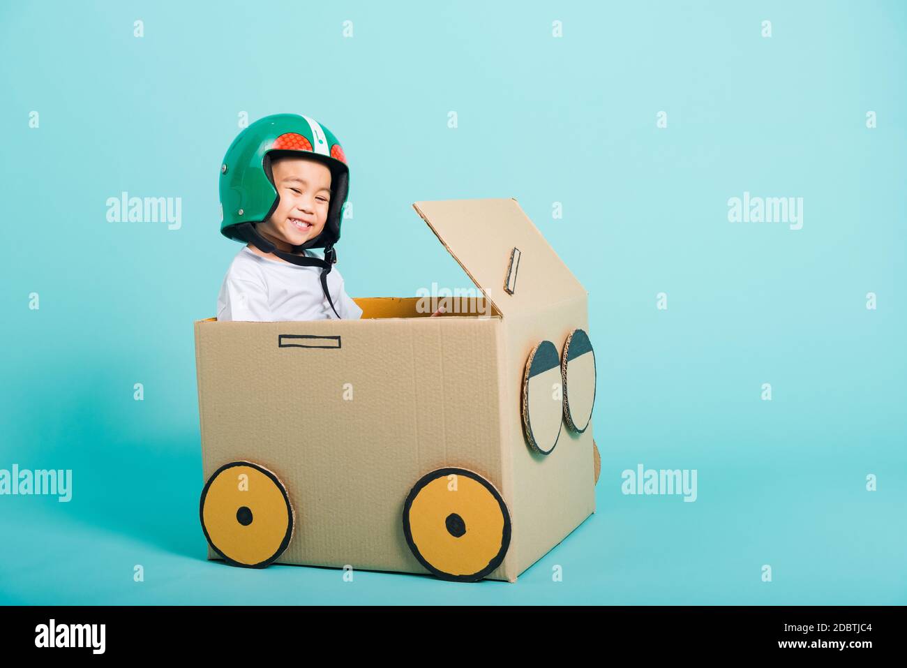 Fröhliche asiatische Kinder Junge mit Helmlächeln beim Fahren Spielauto kreativ durch eine Pappkartonvorstellung, Sommerferienreisekonzept, Studio angeschossen Stockfoto