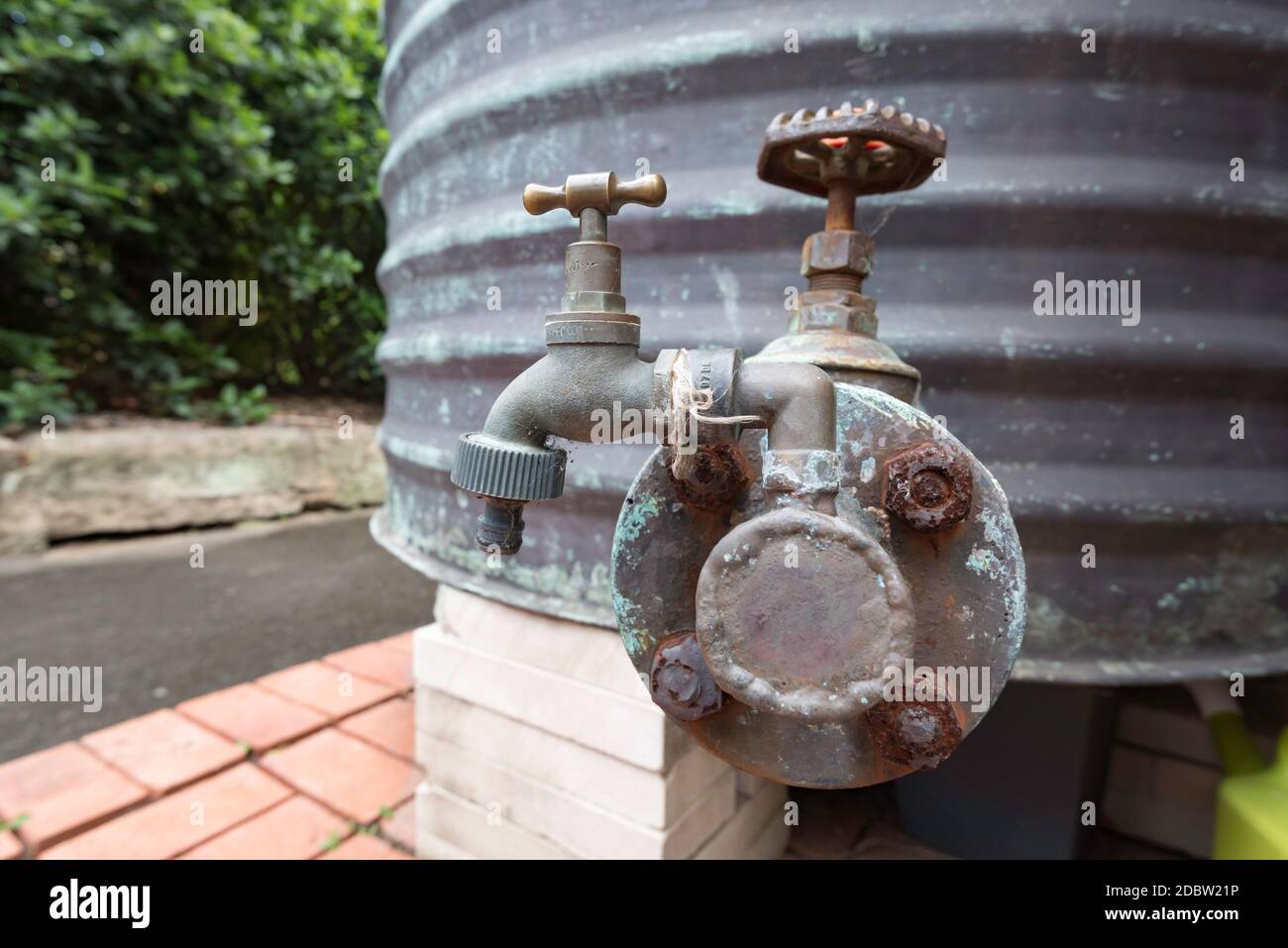 Ein Außenhahn aus Messing, der mit einem ehemaligen Kupfer-Heißwassertank im Dach verbunden ist, wurde hochgetaktet, der jetzt draußen sitzt und Regenwasser von einem nahegelegenen Dach sammelt Stockfoto
