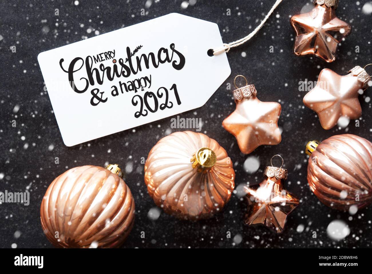 Ein Label mit englischer Kalligraphie Frohe Weihnachten und EIN glückliches 2021. Goldene Weihnachtskugel Ornament Auf Schwarzem Hintergrund Und Schneeflocken Stockfoto