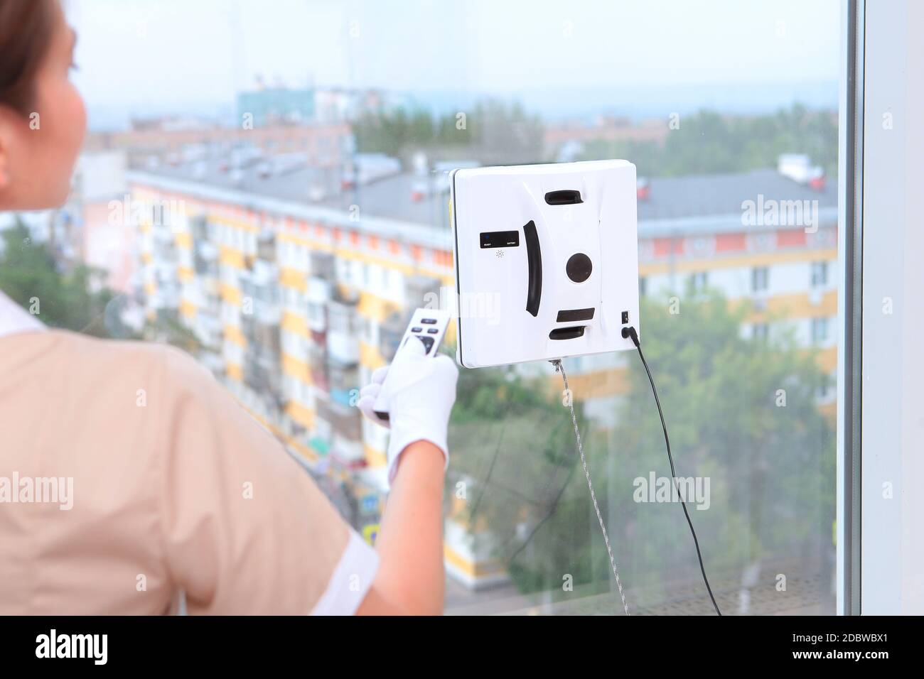 Ein Mädchen in Uniform steuert ferngesteuert einen Roboter, der Windows reinigt. Blick aus dem Fenster. Konzept der Reinigung in einem Hotel oder zu Hause. Reinigung des Hotels Ro Stockfoto