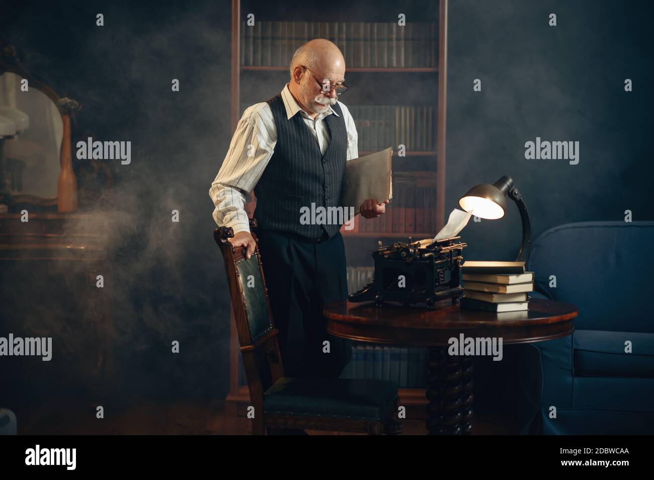 Älterer Schriftsteller arbeitet an Vintage-Schreibmaschine in seinem Heimbüro. Alter Mann in der Brille schreibt Literaturroman Stockfoto