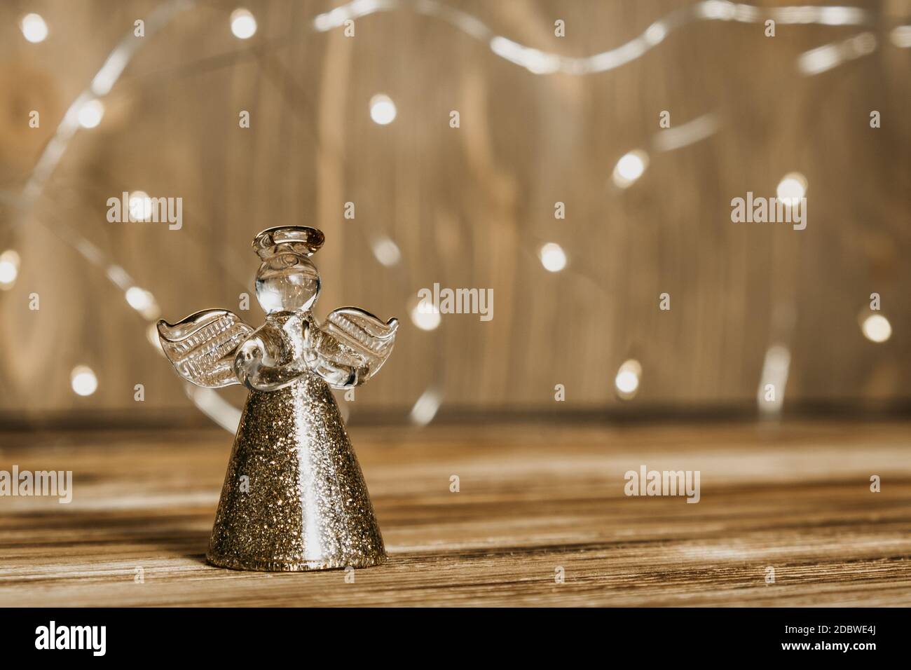 Weihnachtskarte mit einem Engel und einer Girlande auf einem Holzhintergrund. Defokussierten Lichter Hintergrund und Weihnachtsdekorationen. Selektiver Fokus. Nahaufnahme. Stockfoto