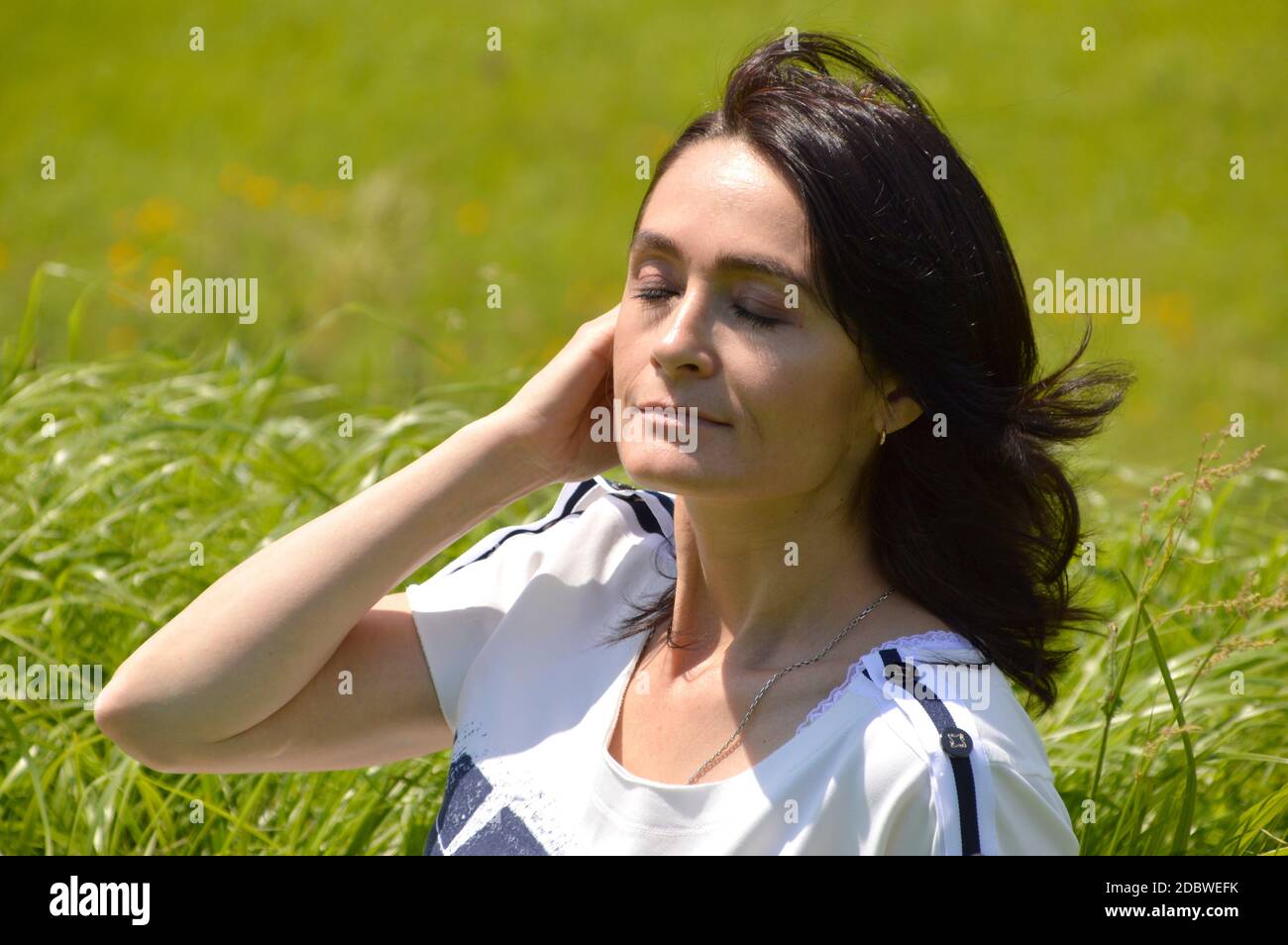 Porträt der 45-jährigen kaukasischen Brünette Frau mit geschlossenen Augen auf einem grünen Feld. Genießen Sie den Sommerhauch Stockfoto