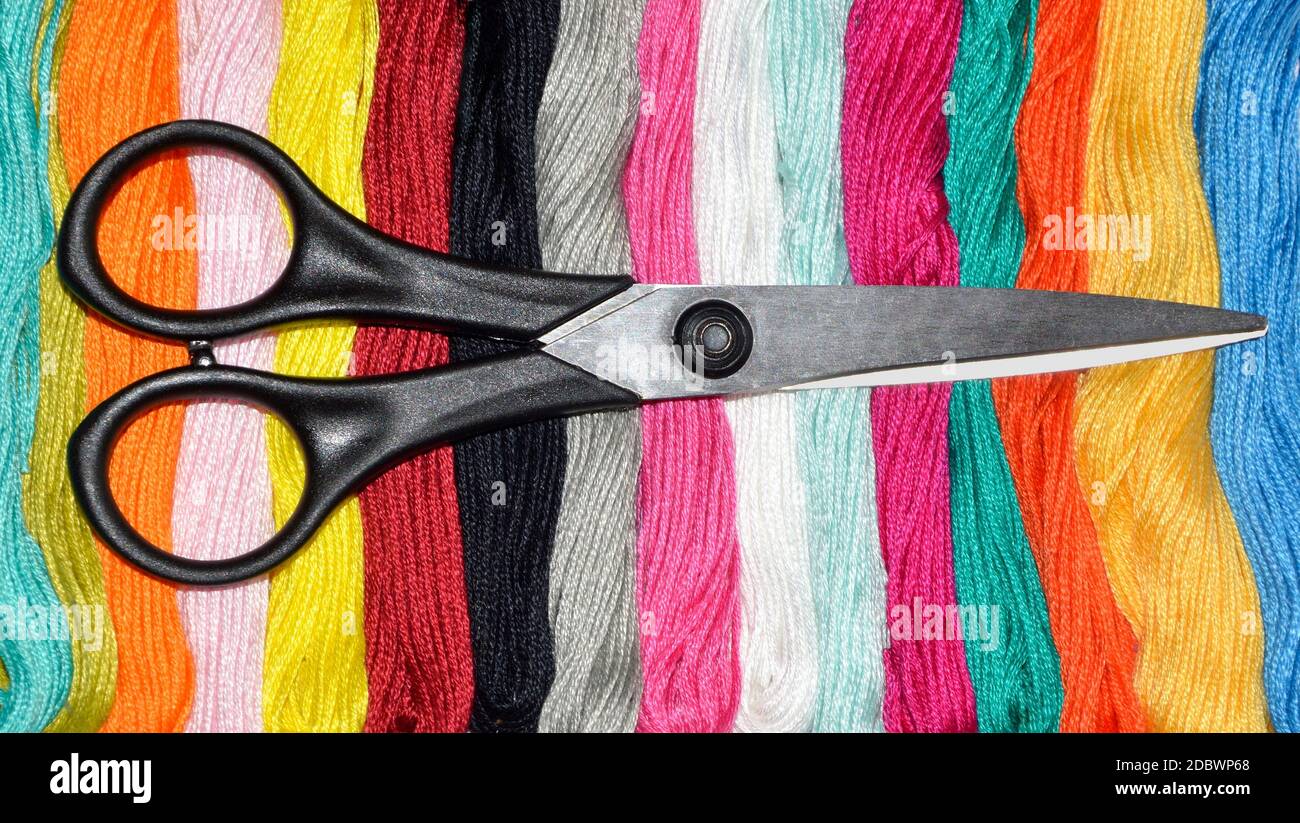 Schwarze Schere auf mehrfarbigen Skeins aus Zahnseide. Auswählen einer Farbe für Nadelarbeit Stockfoto