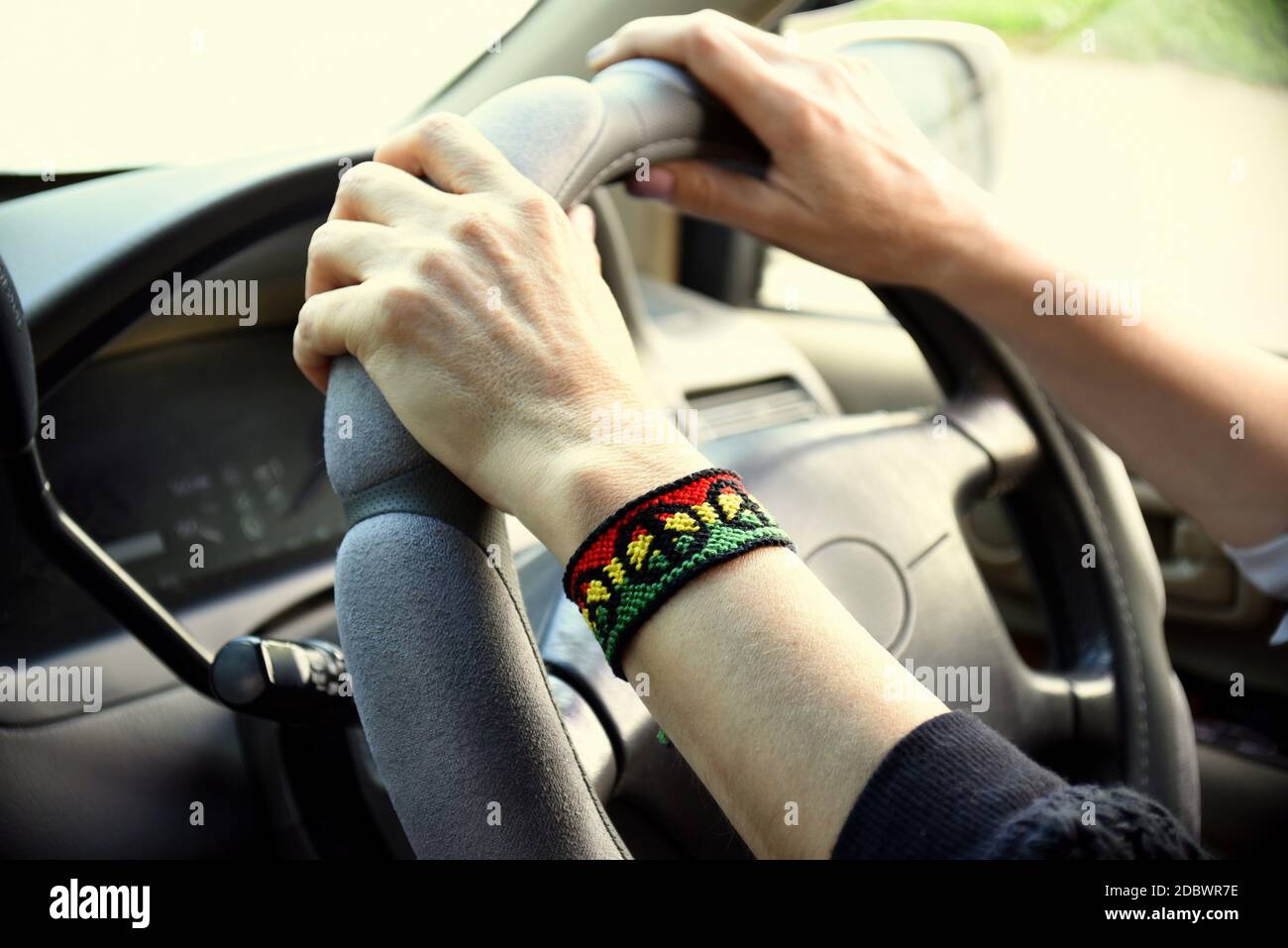 Handgemachtes DIY Freundschaftsarmband mit Rasta Flag-Muster mit einem Friedenssymbol am Handgelenk der Frauen. Hände, die das Lenkrad im Fahrzeug halten. Stockfoto