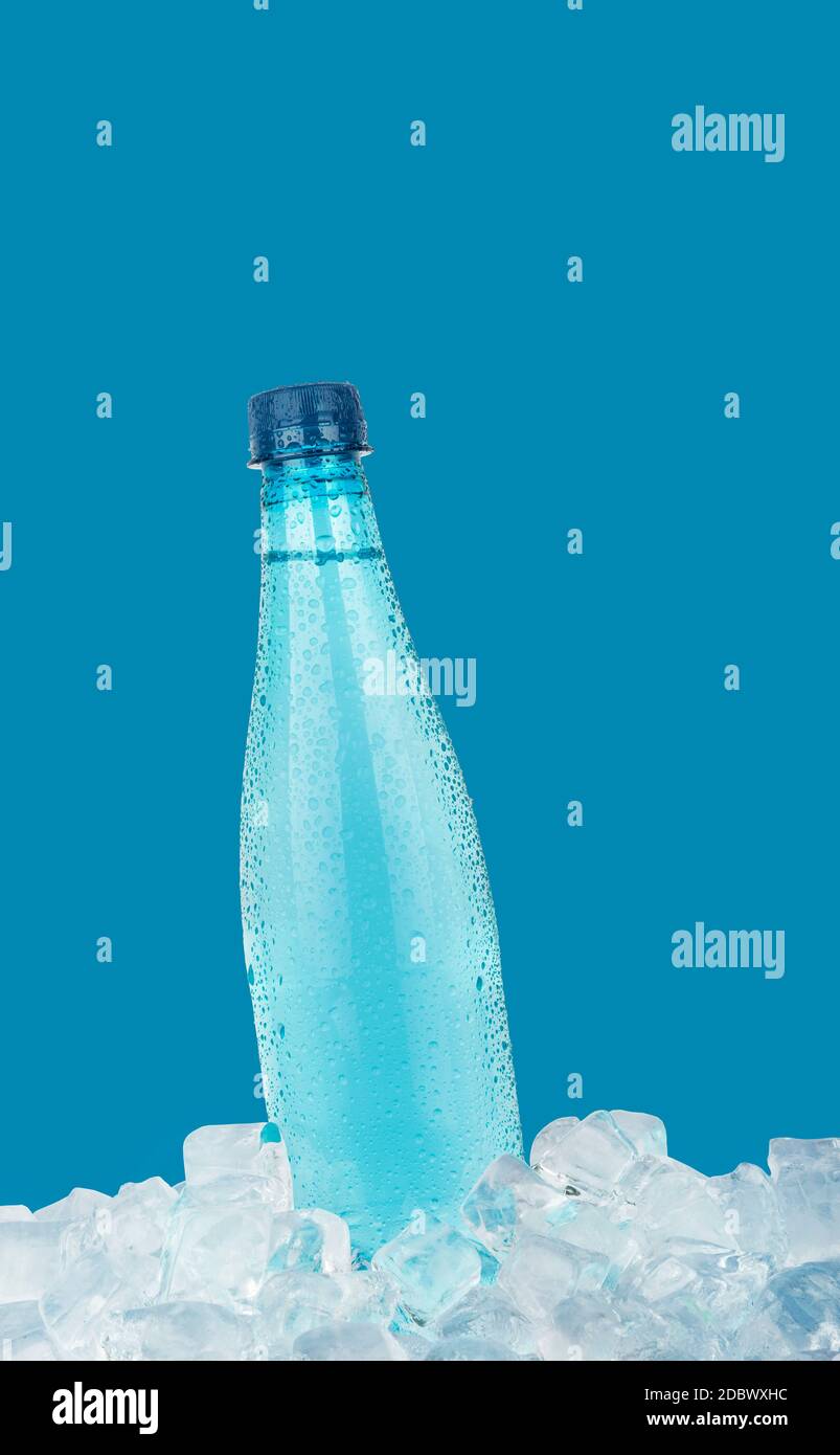 Eine vollständige PET-Kunststoffflasche mit kaltem, noch kühlem Trinkwasser auf Eiswürfeln, isoliert auf blauem Hintergrund, mit niedriger Seitenansicht Stockfoto