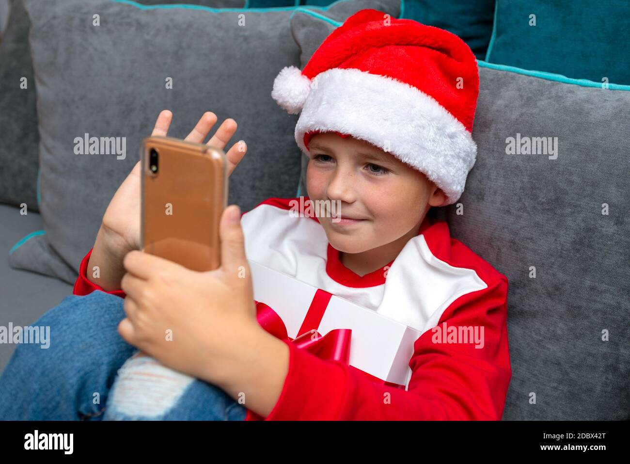 Handsome Kind Junge in Weihnachtsmann Hut sieht Smartphone-Bildschirm, sprechen Sie mit der Familie, Nahaufnahme Bild. Stockfoto