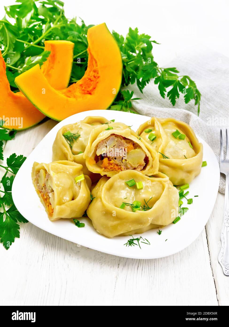 Manty gedämpfte Kuchen mit Hackfleisch und Kürbis, grüne Zwiebeln in einem Teller, Serviette, Petersilie und Gabel auf Holzbrett Hintergrund Stockfoto