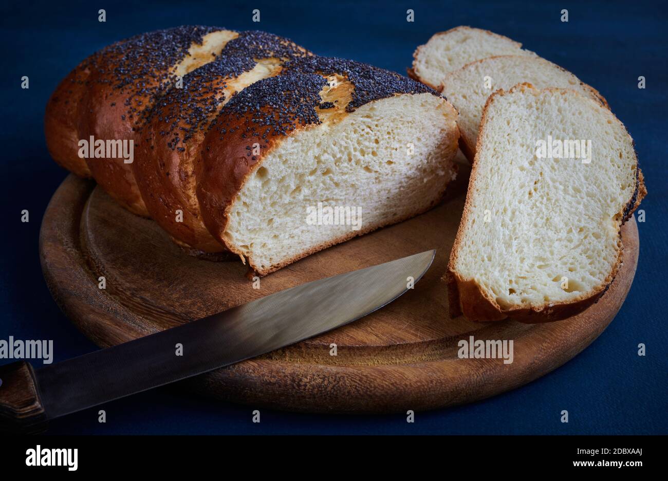 Frisches Weißbrot Brot bestreut mit Mohn auf einem Schneidebrett mit Scheiben und einem Messer, blauer Hintergrund Stockfoto