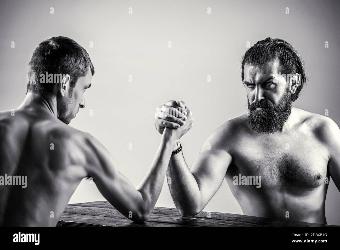 Arme ringen dünne Hand, großer starker Arm im Studio. Zwei Männerhände umklammten Arm Wrestling, stark und schwach, ungleiche Übereinstimmung. Schwarz und Weiß Stockfoto