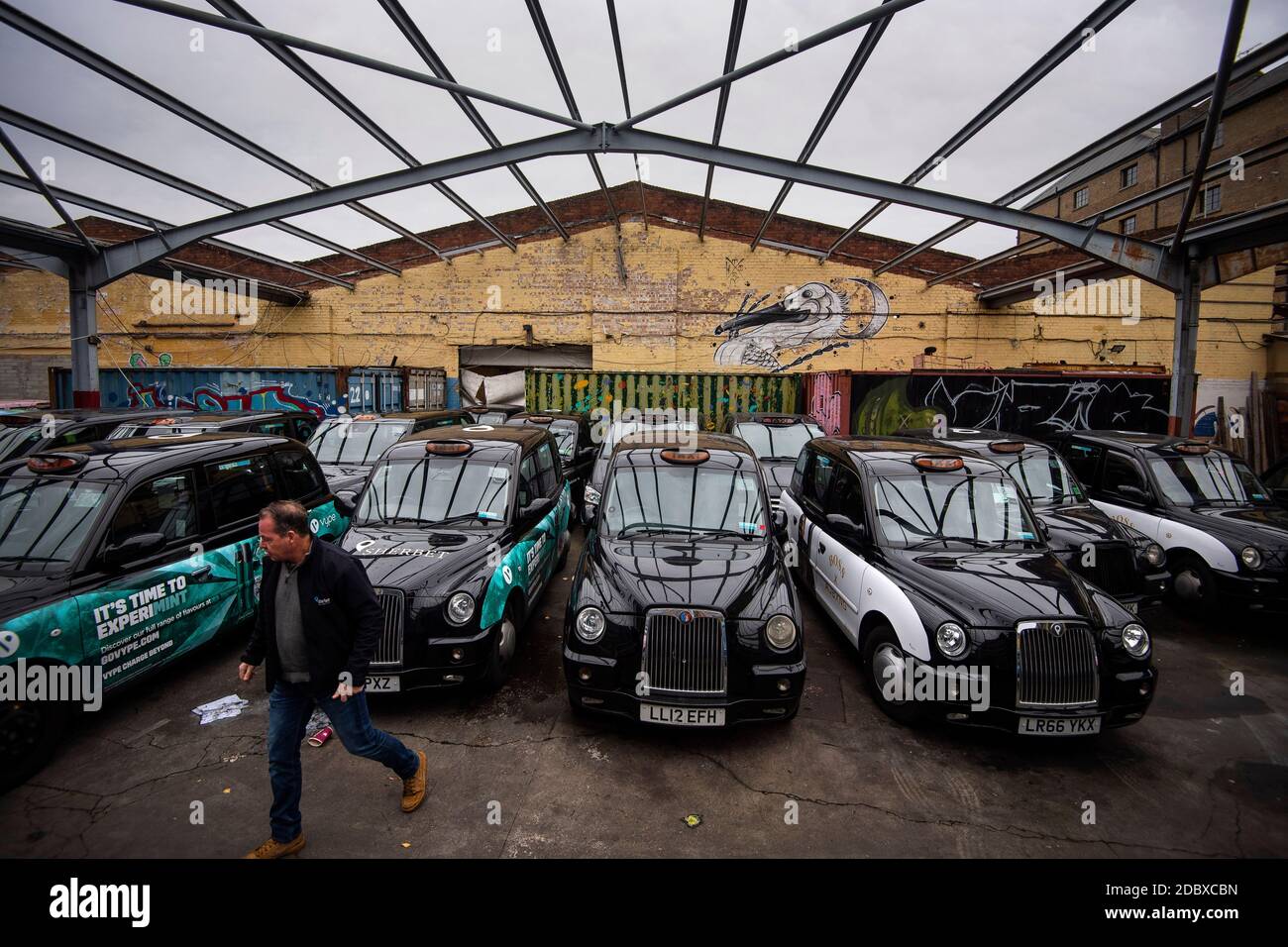 Ein Mitarbeiter geht durch einen Hof mit schwarzen Taxis in Sherbet London im Osten Londons, wo ein großer Teil seiner Mietflotte von Londoner Taxis aufgrund eines starken Nachfragerückgangs aufbaut, da die Beschränkungen des Coronavirus die Reise- und Büroarbeit weiter reduzieren. Stockfoto