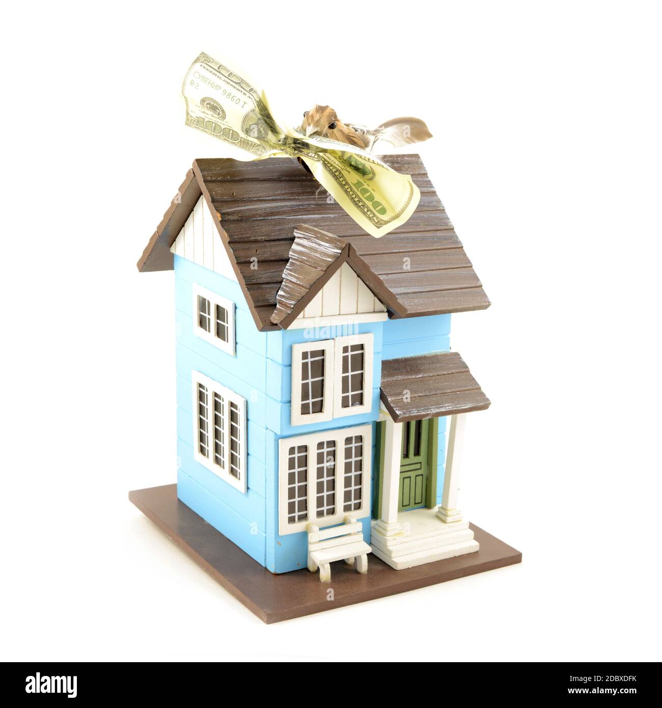 Ein konzeptuelles Bild mit einem kleinen Vogel, der einen Hundert-Dollar-Schein im Schnabel hält, während er sich auf einem Miniaturhaus ausruht. Stockfoto