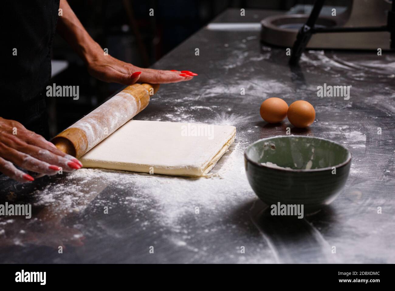 Der Küchenchef bereitet Gebäck in einer professionellen Küche zu. Den Teig kneten. Eier, Mehl, Nudelholz. Dunkler Hintergrund. Stockfoto