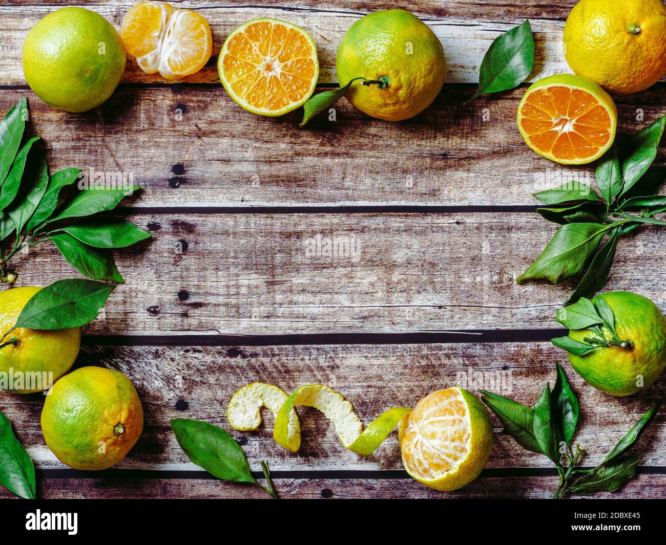 Grüne Mandarinen auf altem Holzhintergrund. Frische reife Hälfte, ganze und geschälte grüne Mandarinen mit Blättern, Draufsicht oder flache Lage. Platz für Text oder Design kopieren. Stockfoto