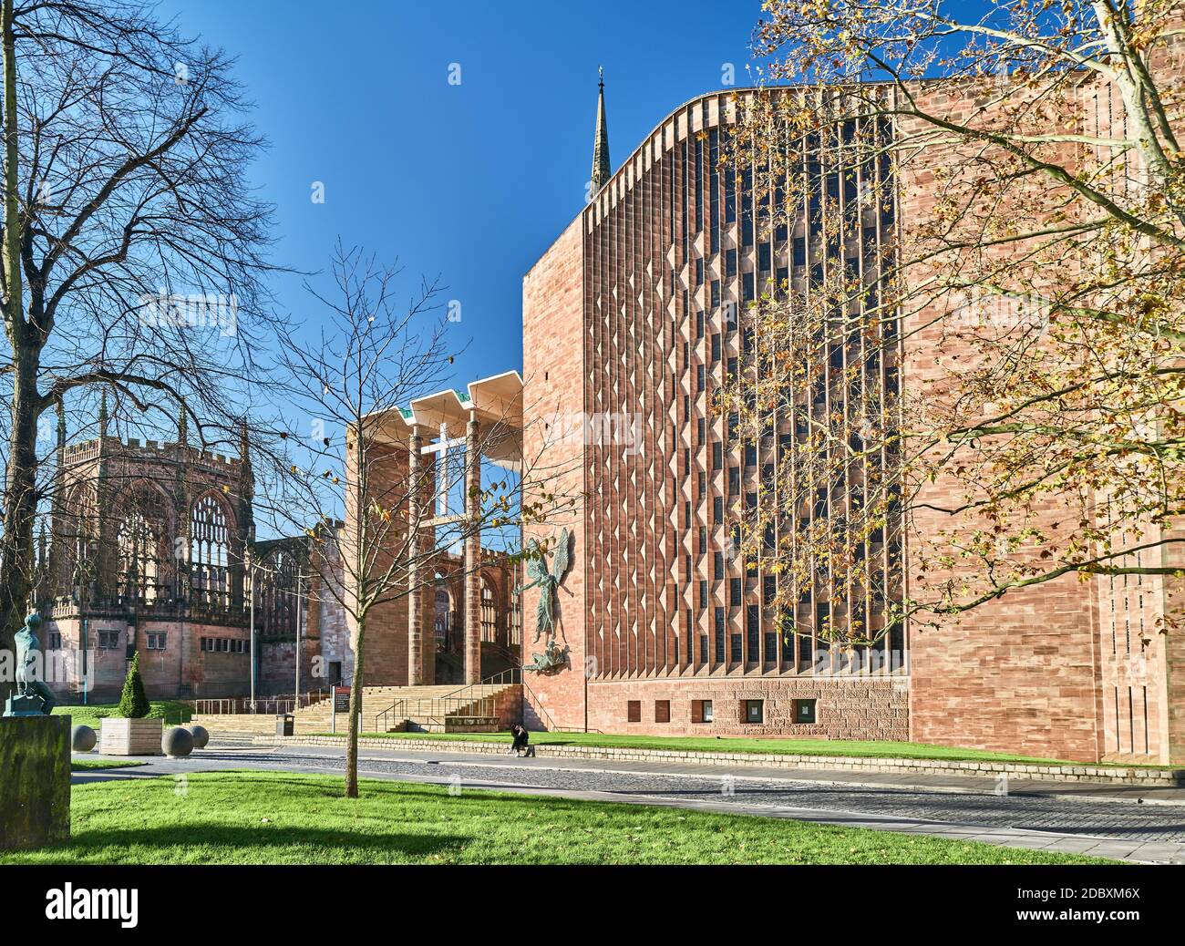 An einem sonnigen Herbsttag sitzt auf der niedrigen Mauer außerhalb der Ostseite und des Tauffensters der neuen christlichen Kathedrale in Coventry eine einköpfige Person. Stockfoto