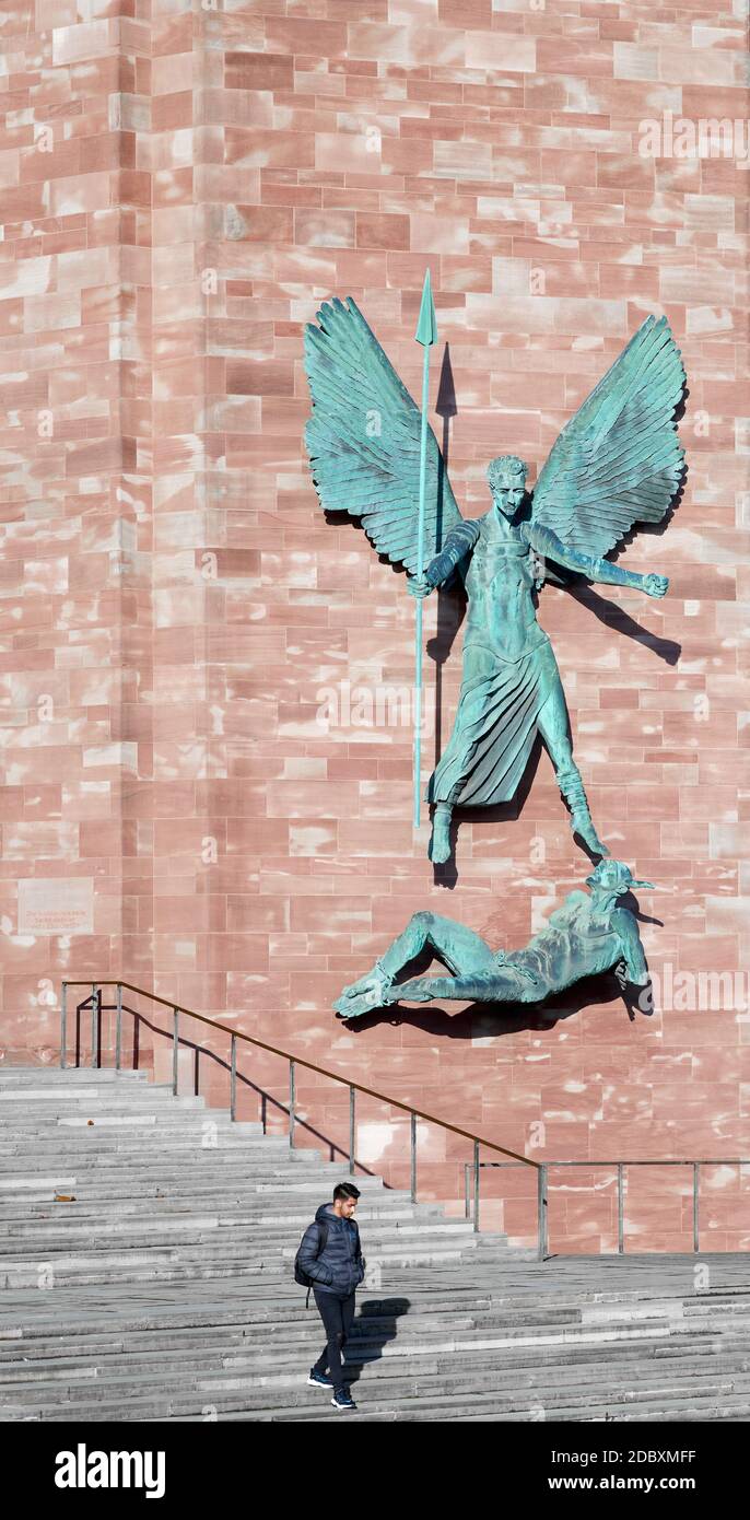 Ein männlicher Student steigt in der neuen christlichen Kathedrale in Coventry, England, unter die Skulptur von Jacob Epstein von St. Michael und dem Teufel. Stockfoto