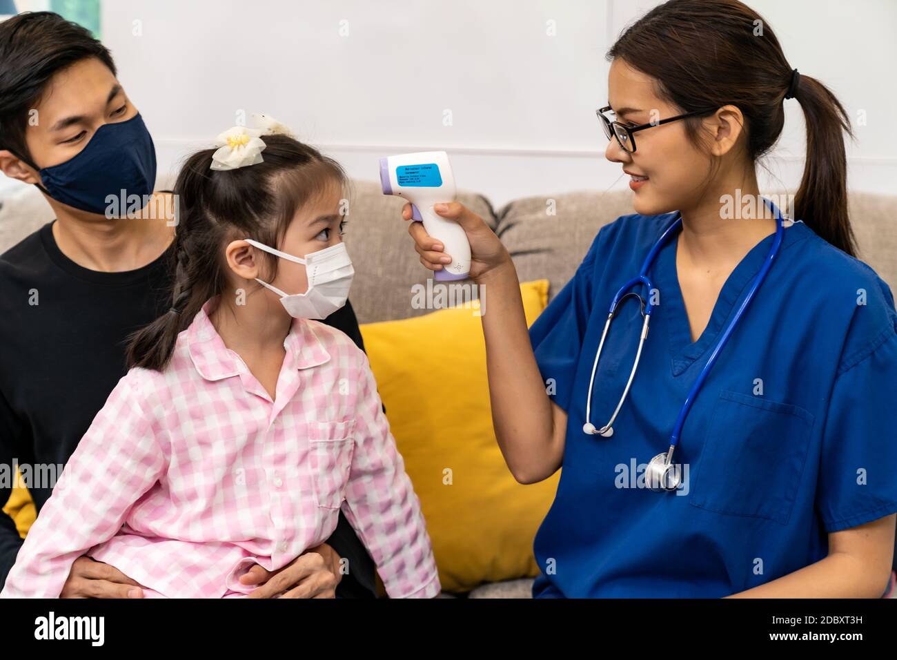 Asiatische weibliche Arzt verwenden Infrarot-Thermometer, um Temperatur zu kleinen Mädchen Kind sitzen mit ihrem Vater im Wohnzimmer zu nehmen, während Arzt zu Hause besuchen. Zu Hause Stockfoto