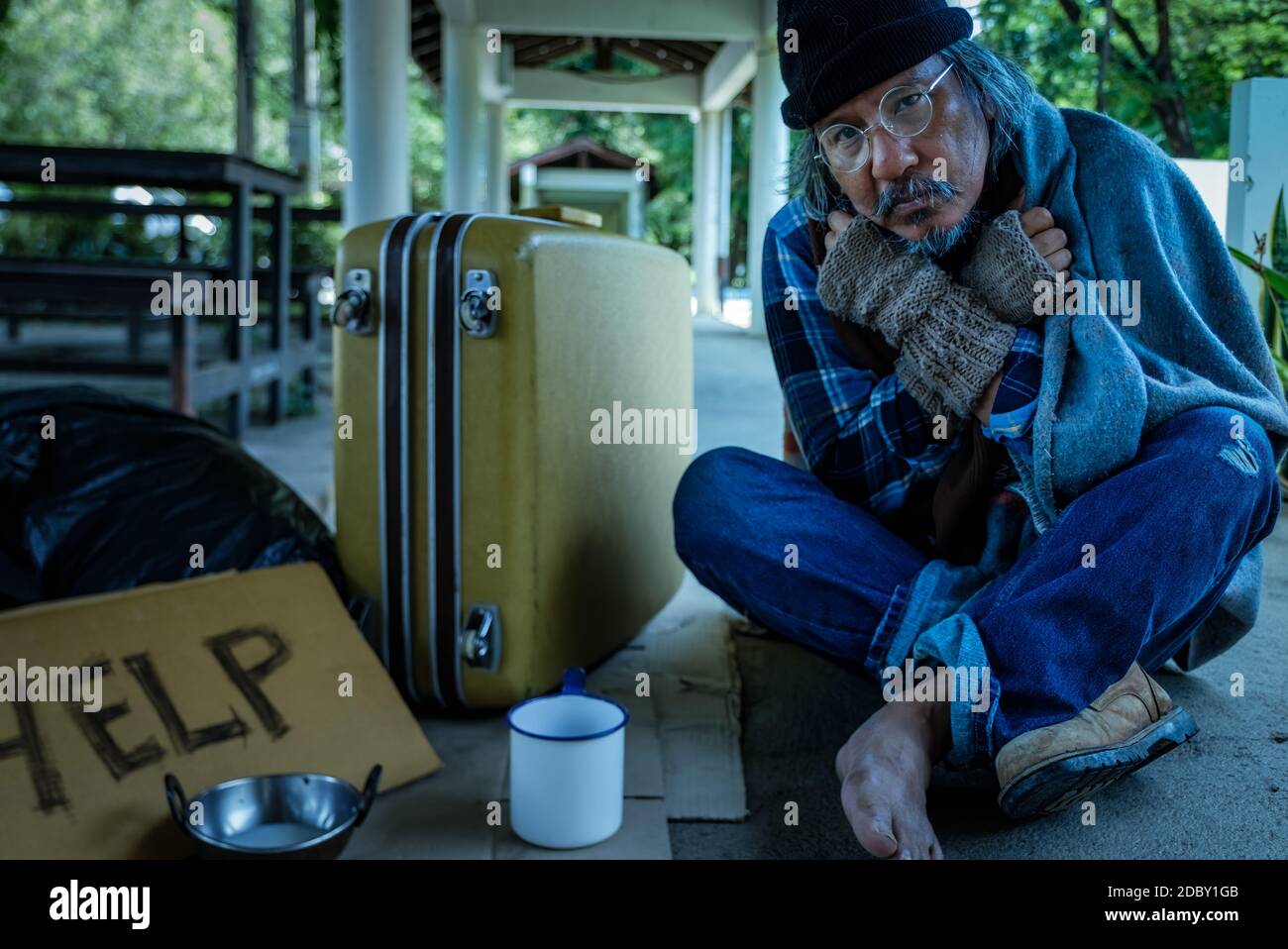 Obdachloser sieht müde und erschöpft aus, während er auf Hilfe von Passanten wartet. Er lebt am Bürgersteig und bittet Menschen um Hilfe. Stockfoto