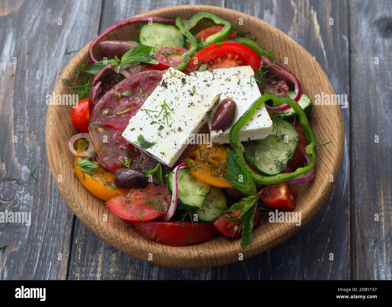 Hausgemachter griechischer Salat aus Tomaten, Gurken, Paprika, Käse, Oliven und Gemüse in einer Holzschüssel auf einem Holztisch. Gesundes, leckeres Essen Stockfoto