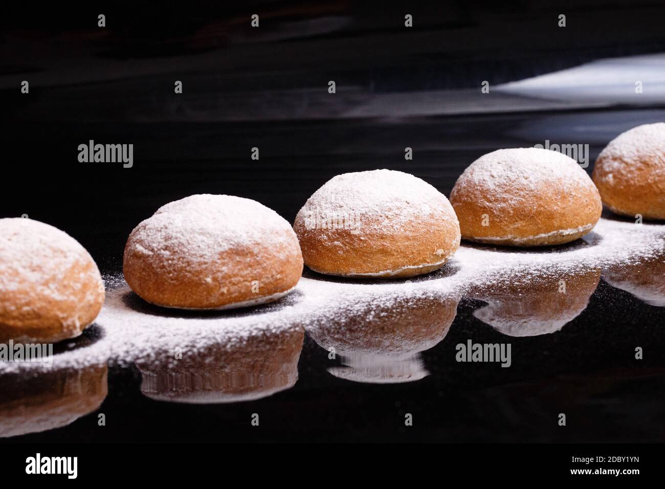 Backen auf schwarzem Hintergrund. Weiße Brötchen mit Pulver und Mehl bestreut. Backen zu Hause mit Pulver bestreut. Stockfoto