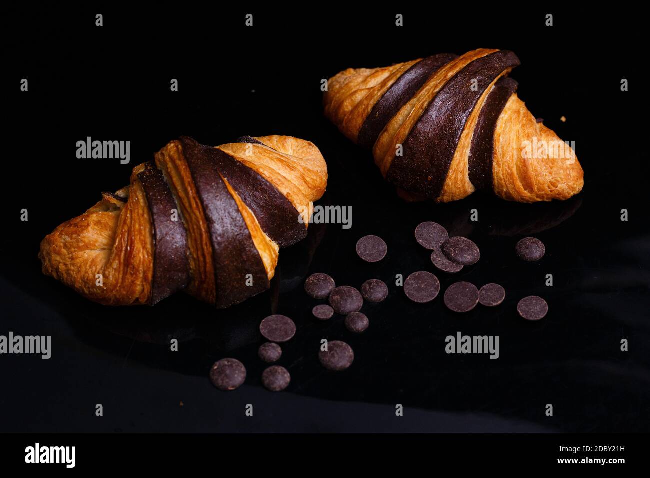 Croissants mit Schokolade. Hausgemachtes Gebäck, Croissants mit Schokolade und Rosinen aus Schokolade. Foto von Croissants auf schwarzem Hintergrund Stockfoto