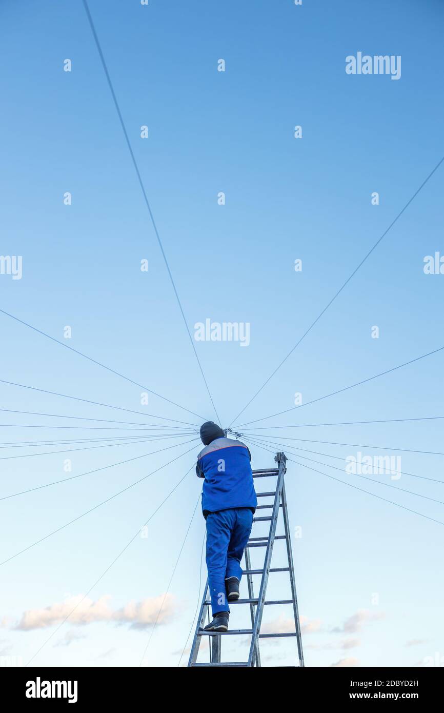 Elektriker repariert elektrische Verkabelung auf dem Dach eines Hochhauses, das auf der Treppe gegen den blauen Himmel steht. Speicherplatz kopieren Stockfoto