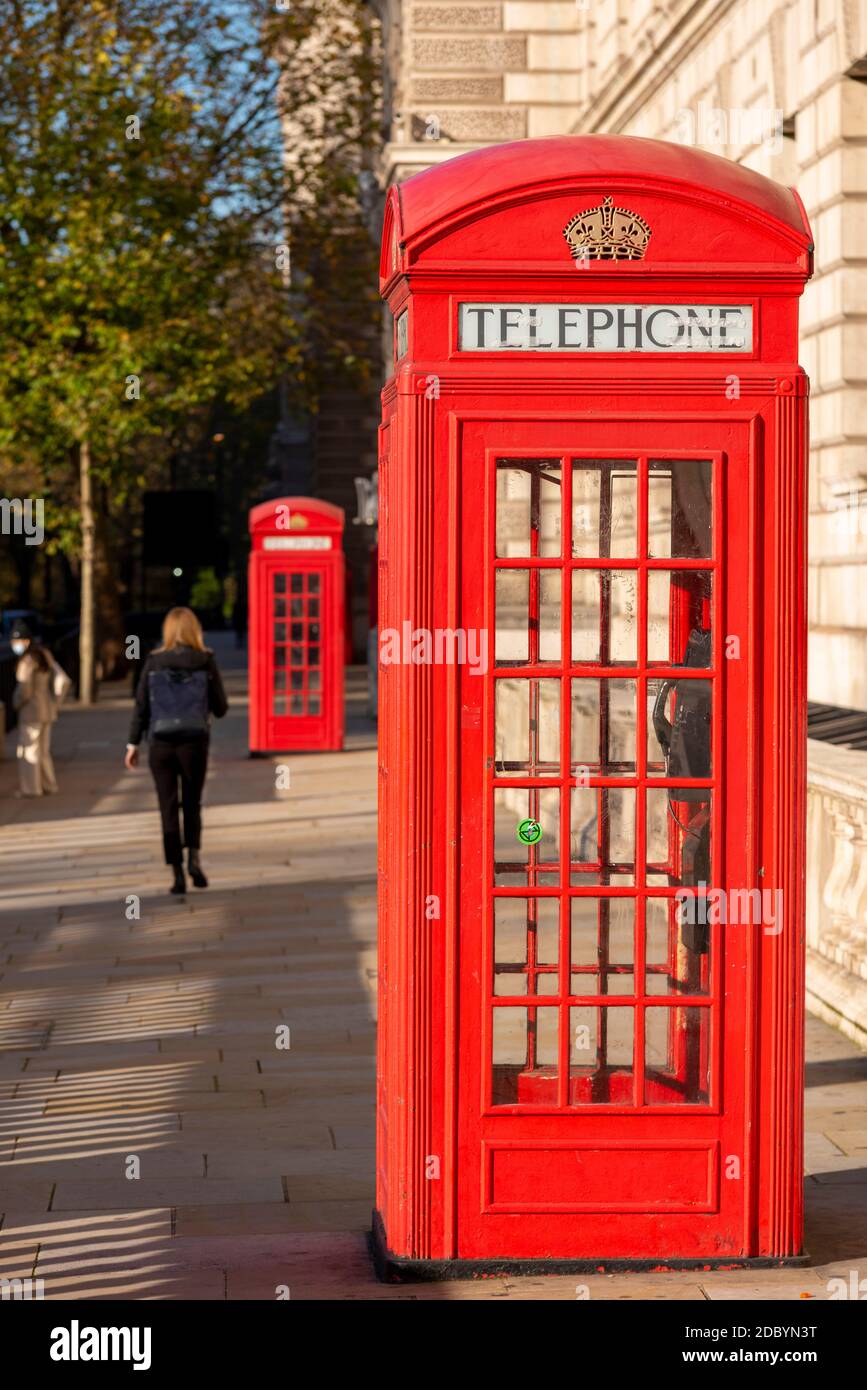 Ikonische rote Londoner Telefonzellen in Westminster, London, Großbritannien. Frau, die vorbeigeht. Rote Telefonbox. Heller sonniger Tag mit wenigen Menschen im Lockdown Stockfoto