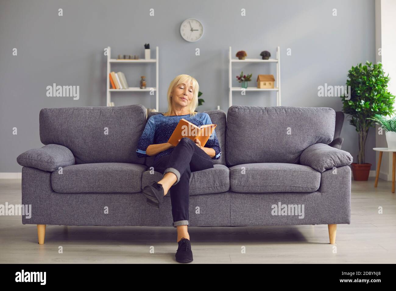 Portrait einer fokussierten älteren Frau, die auf einem Sofa sitzt und ein Interessantes Buch liest. Stockfoto