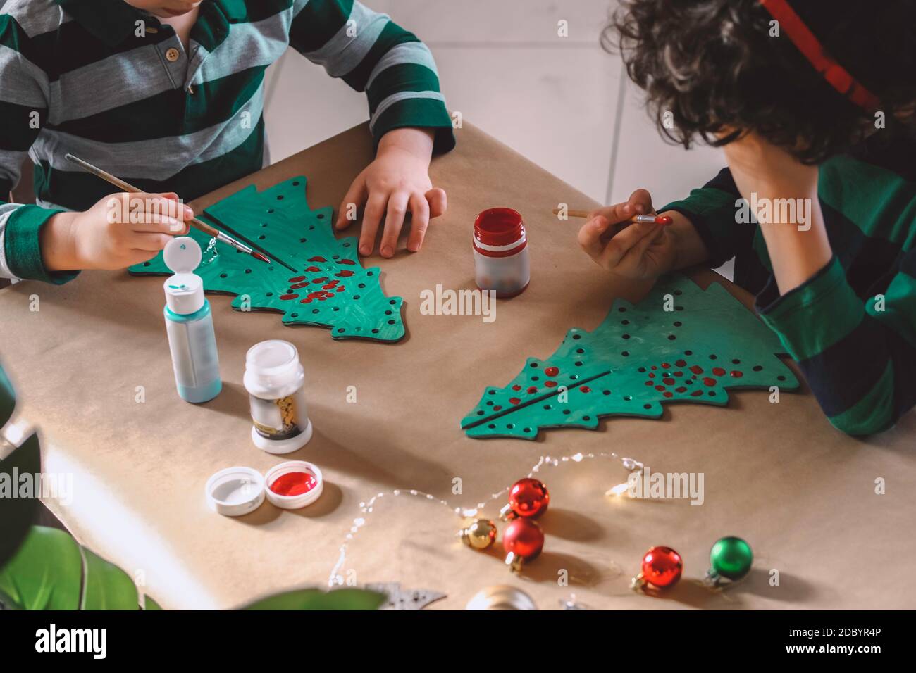 Zwei kleine Kinder machen weihnachtsdekorationen und Postkarten und malen hölzerne Weihnachtsbäume. Stockfoto