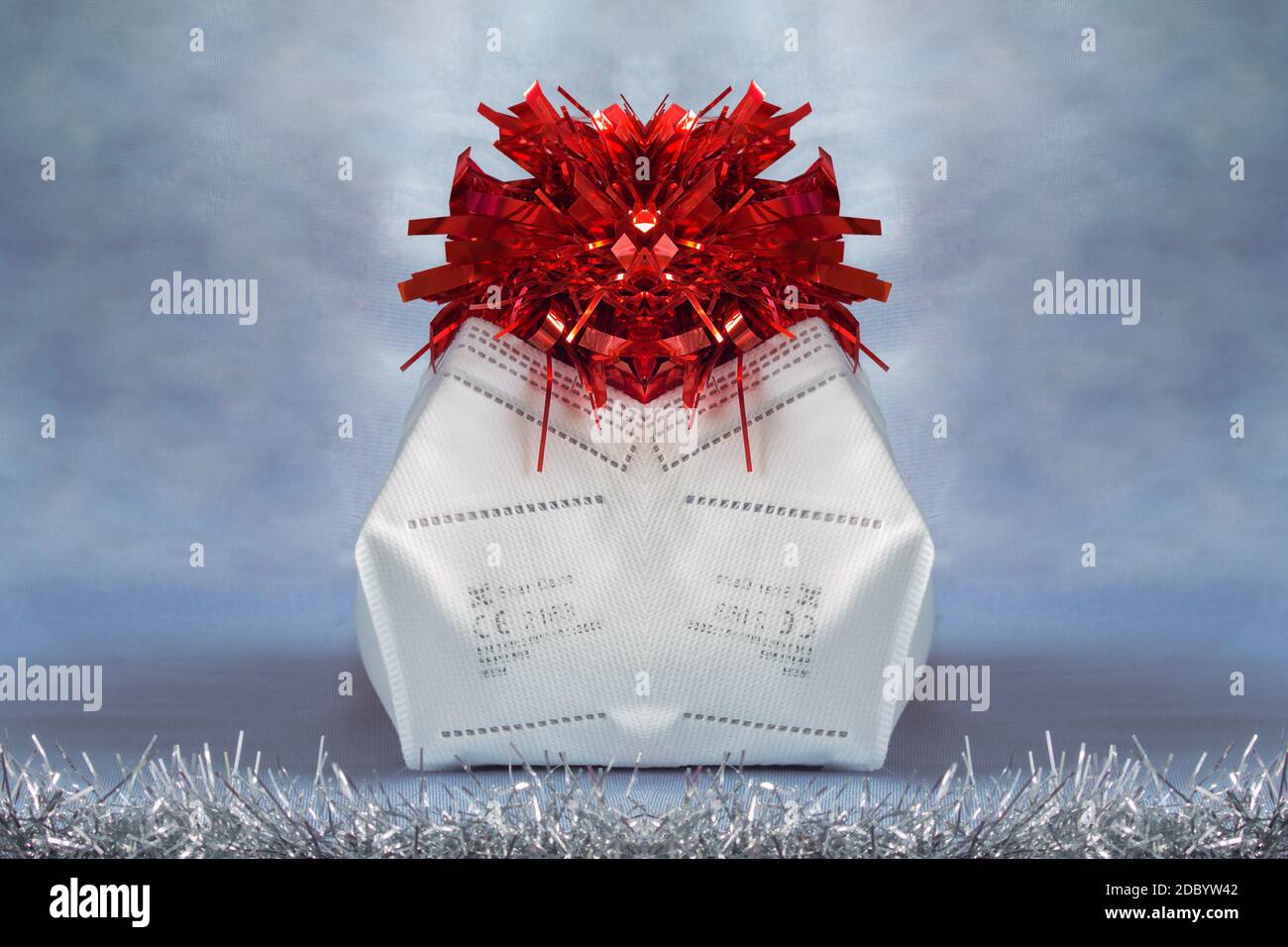 Schutzmaske recycelt und gewaschen als Verpackung für Weihnachtsgeschenke. Original Tasche mit rotem Lametta auf einem bemalten Winter Tuch Hintergrund verziert. Neu Stockfoto