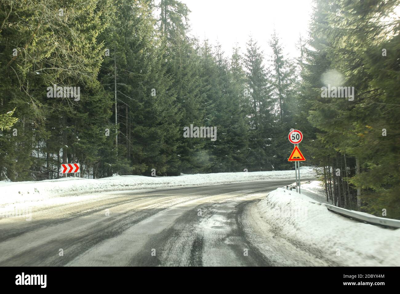 Treiber Blick auf scharfe Kurve der Straße, teilweise mit Schnee im Nadelwald bedeckt, mit starken blendendem Sonnenlicht. Tempo 50 und Stößen zu Il Stockfoto