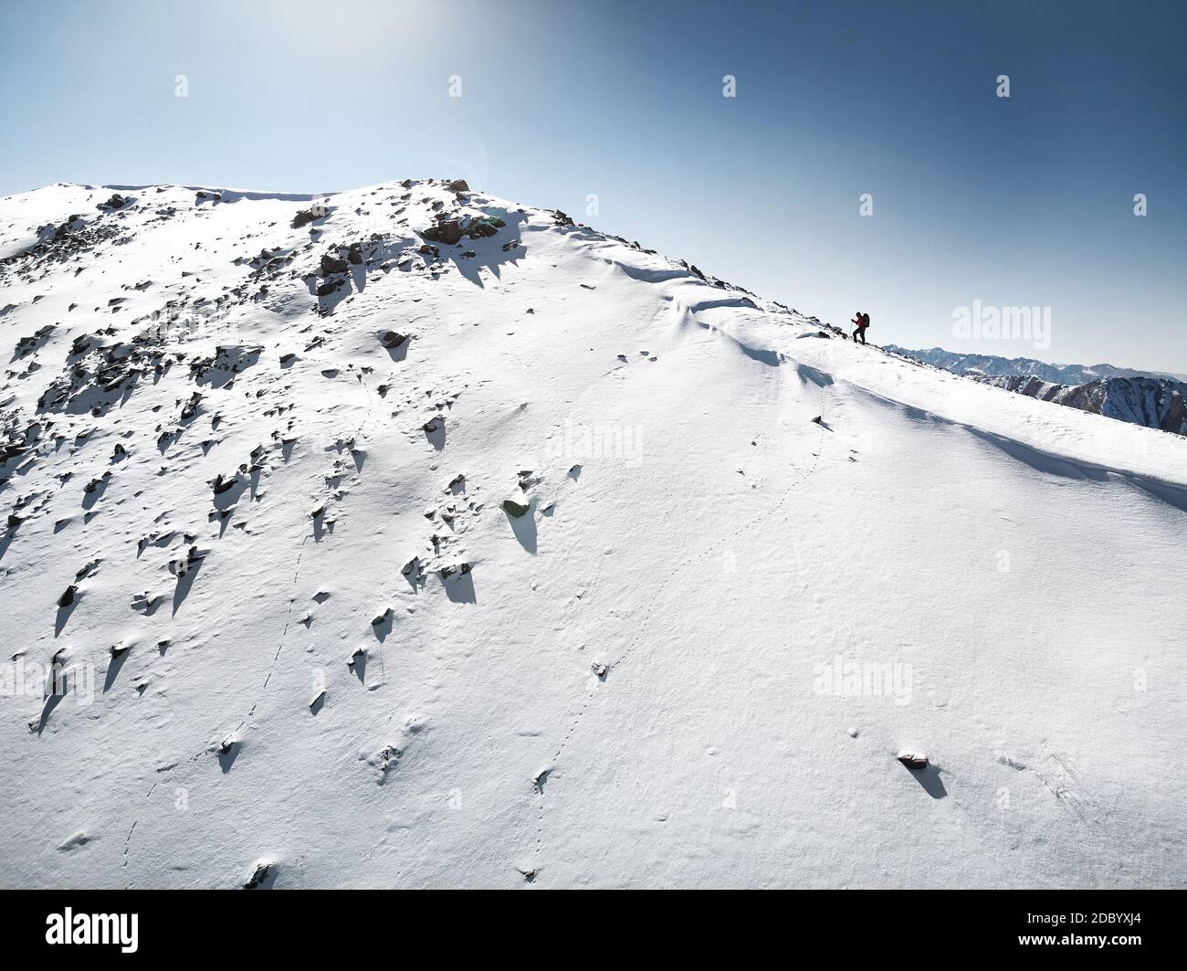 Seitenansicht des Winterberggipfels und kleiner Mann klettert auf dem Schneepfad. Winter Outdoor-Aktivität und Risiko-Konzept. Stockfoto