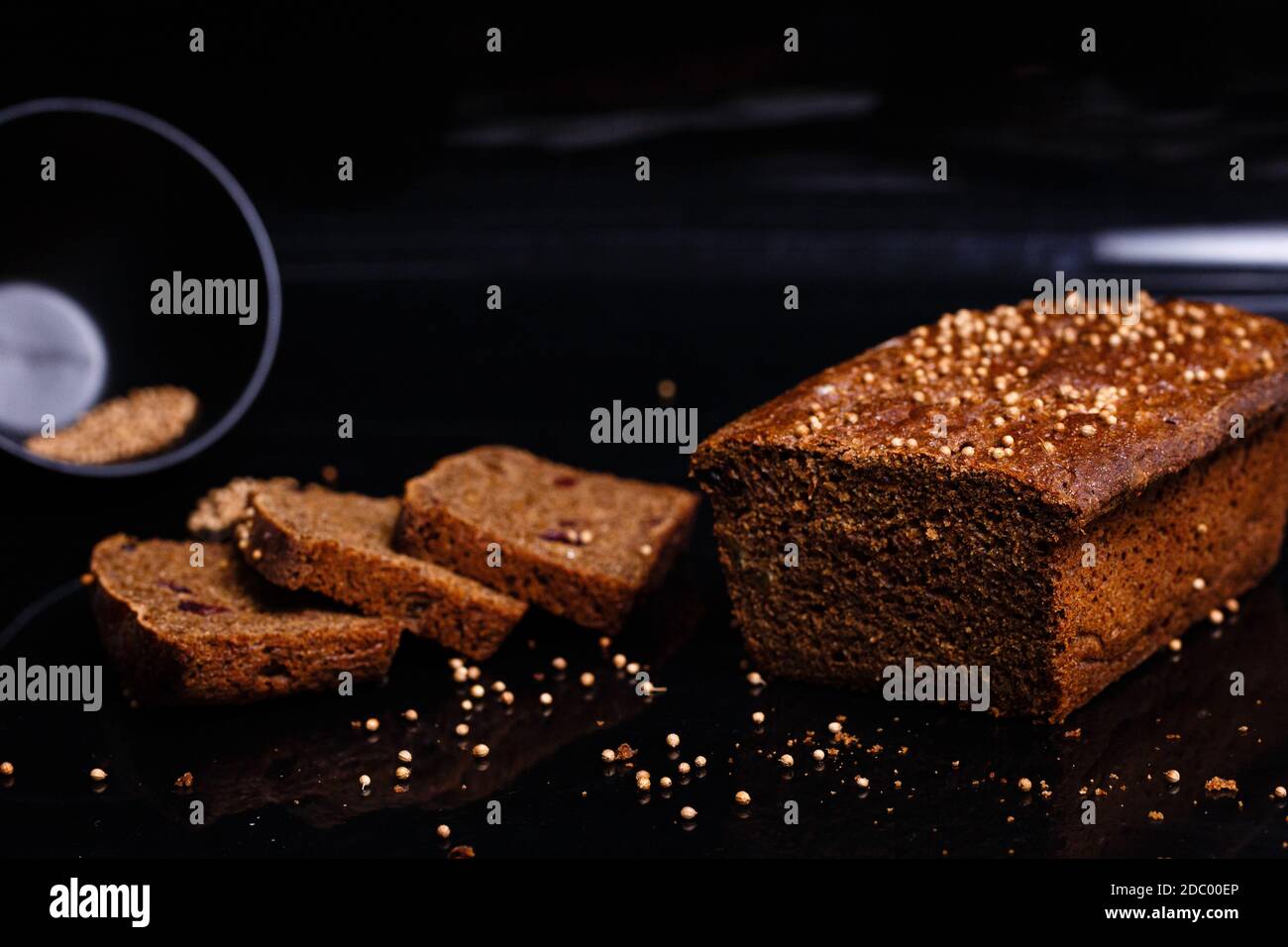 Hausgemachtes schwarzes Brot auf schwarzem Hintergrund. Foto im Abschnitt. Das Mädchen schneidet Brot mit einem Messer. Stockfoto