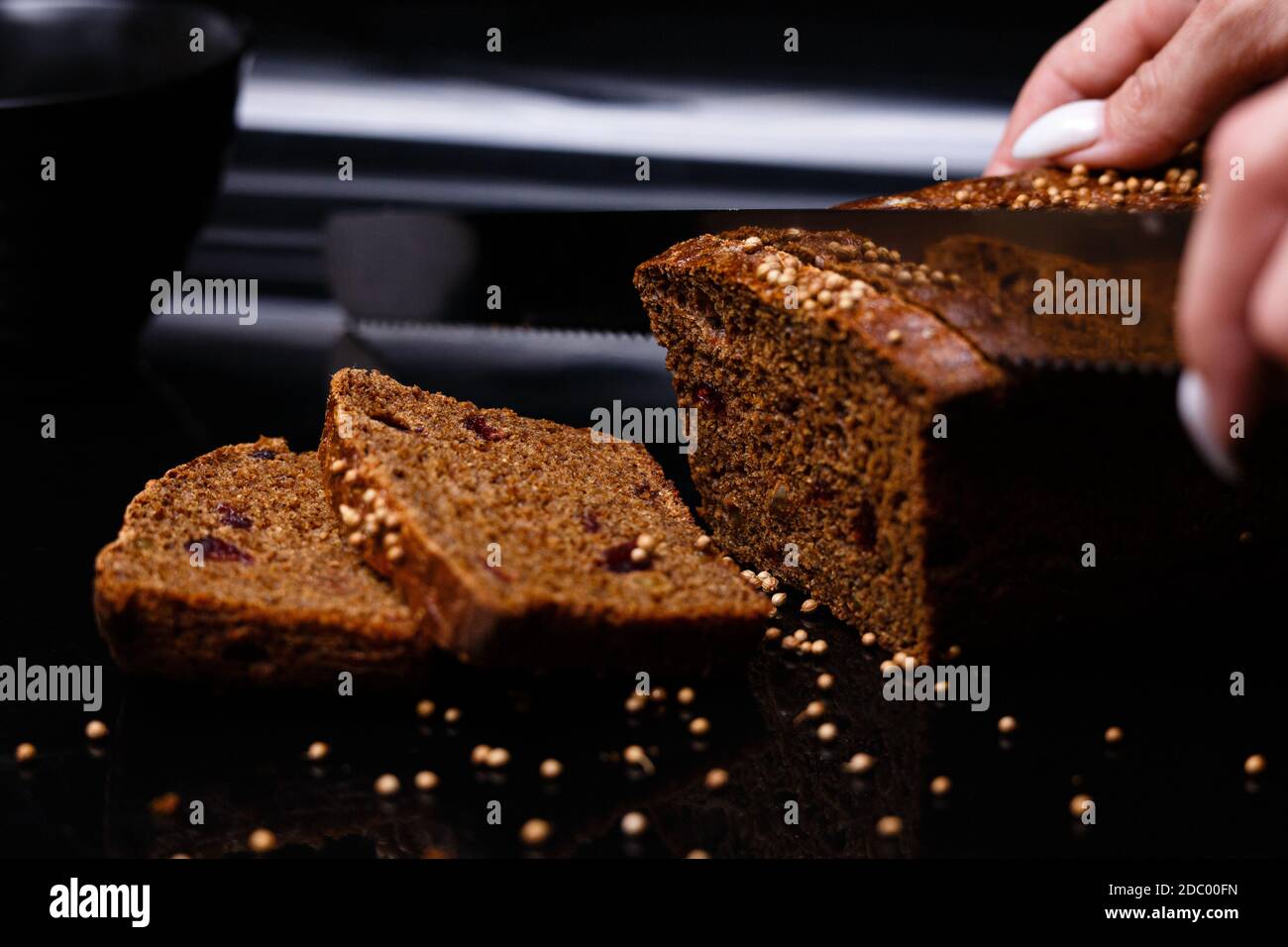 Hausgemachtes schwarzes Brot auf schwarzem Hintergrund. Foto im Abschnitt. Das Mädchen schneidet Brot mit einem Messer. Stockfoto