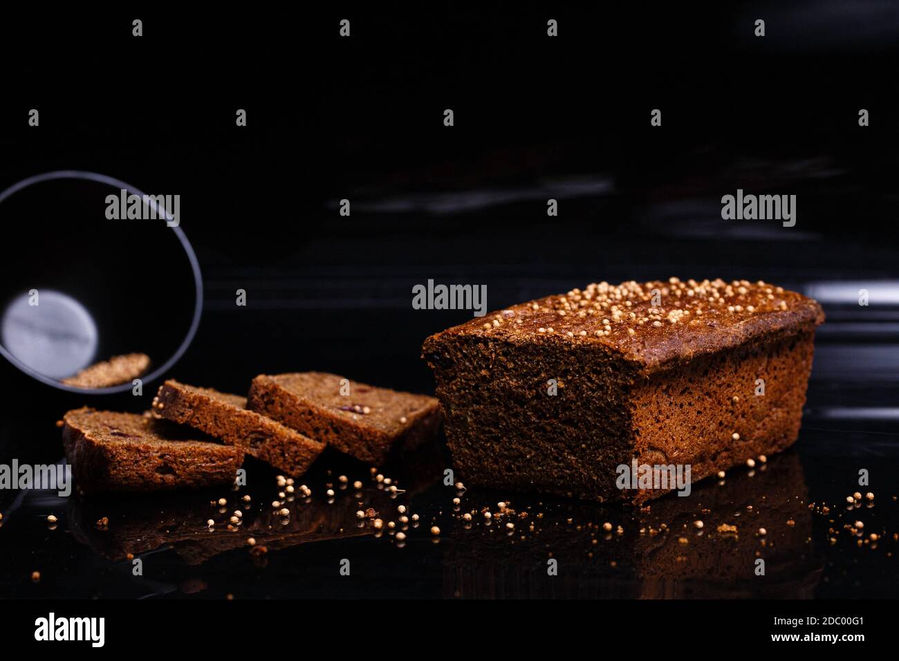 Hausgemachtes schwarzes Brot auf schwarzem Hintergrund. Foto im Abschnitt. Das Mädchen schneidet Brot mit einem Messer. Stockfoto