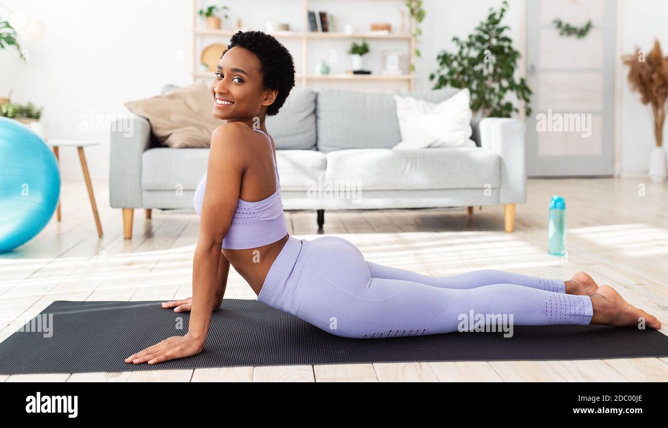 Fit junge schwarze Frau üben Yoga auf Sportmatte zu Hause, so dass Kobra Pose Stockfoto