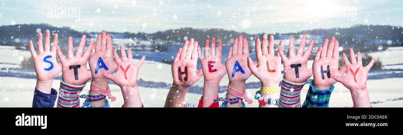 Kinder Hände Halten Bunte Englisch Wort Gesund Bleiben. Verschneite Winter Hintergrund Mit Schneeflocken Stockfoto