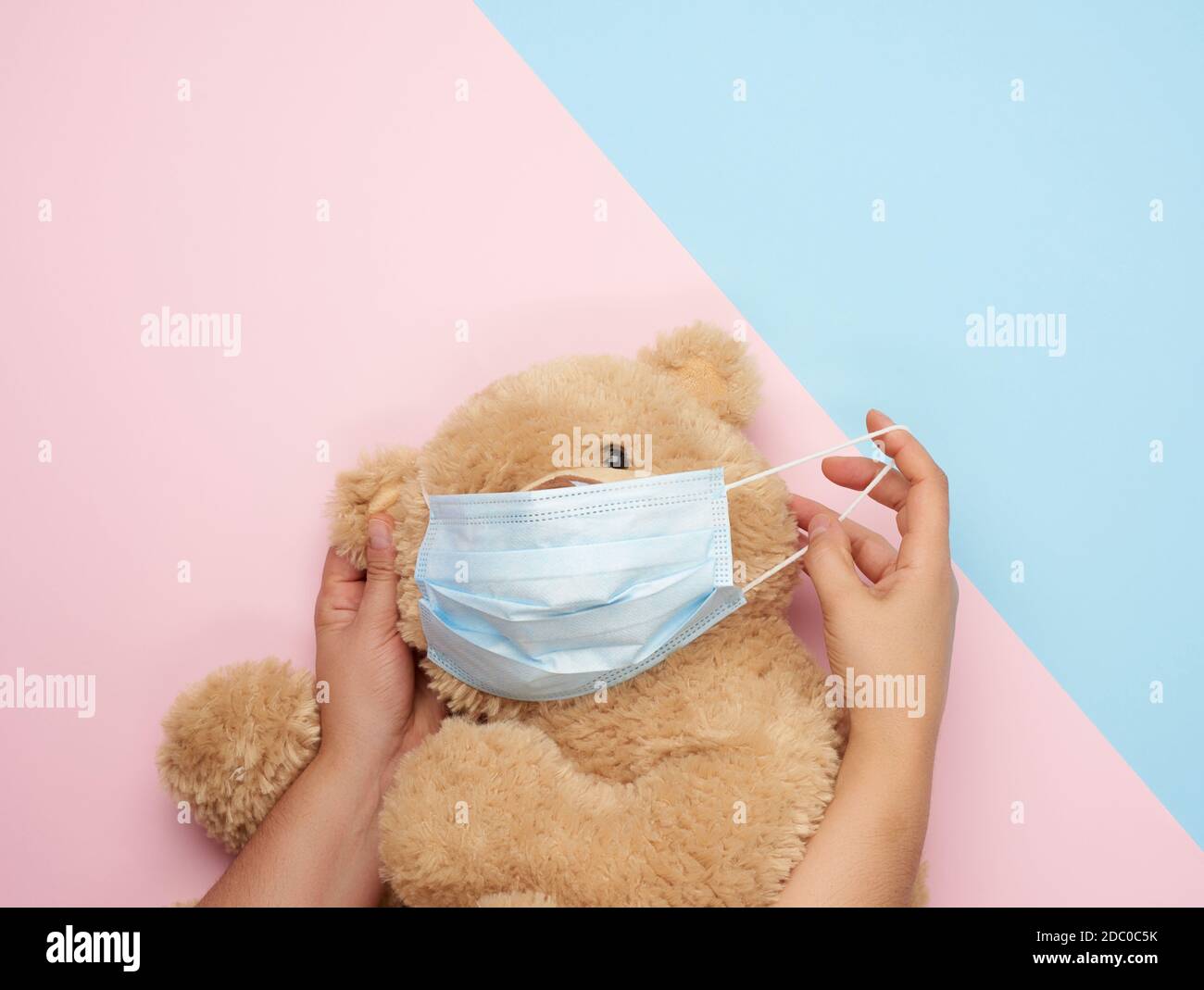 Großer Teddybär in medizinischen Masken auf einem blau-rosa Hintergrund, Konzept des Schutzes vor Atemwegserkrankungen, Virus und individuellen Atemschutz Stockfoto