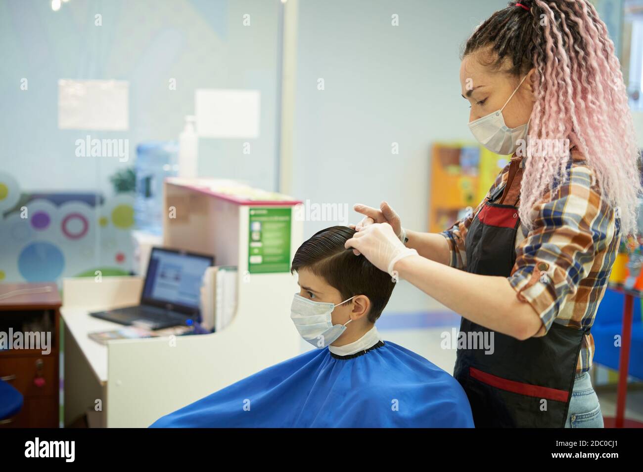 Meister Friseur und ein Junge mit medizinischen Masken machen ein Haarschnitt während einer viralen Pandemie Stockfoto
