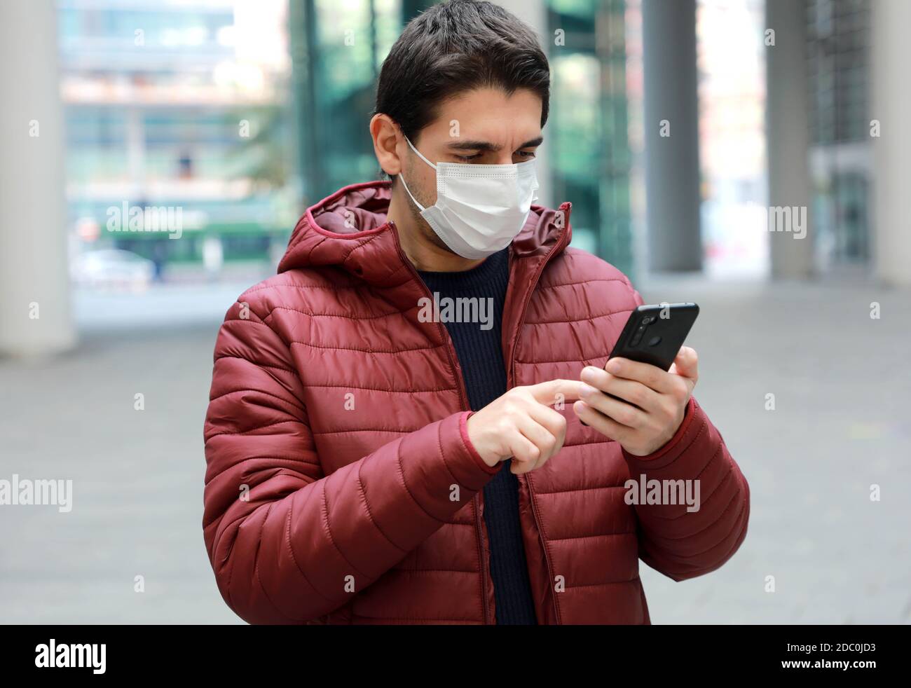 Mann trägt chirurgische Maske mit Smartphone-App in der modernen Stadt Stockfoto