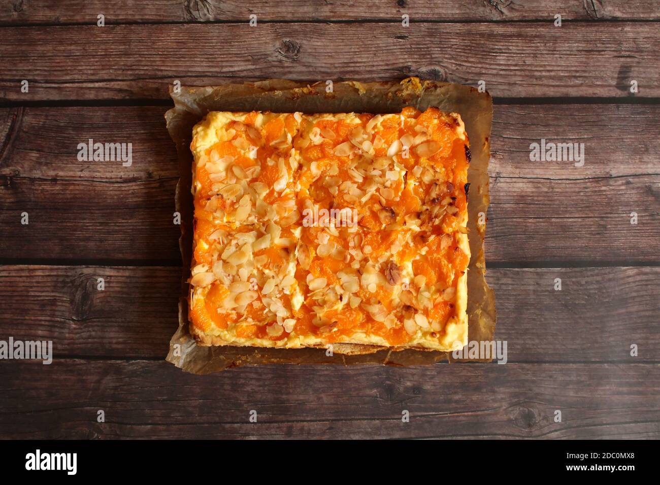 Frisch aus dem Ofen: Ein selbstgebackener deutscher Orangenkäsekuchen auf einem rustikalen Holztisch. Stockfoto