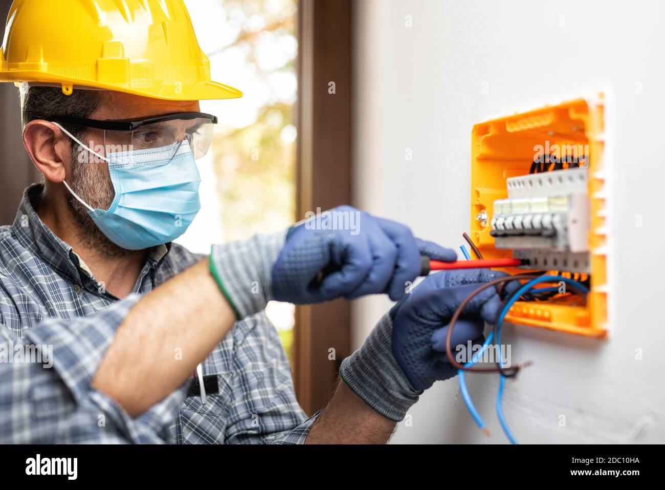 Elektriker bei der Arbeit an einem elektrischen Panel mit Helm, Schutzbrille und Handschuhe geschützt; tragen Sie die chirurgische Maske, um die Ausbreitung von Coronavirus zu verhindern Stockfoto