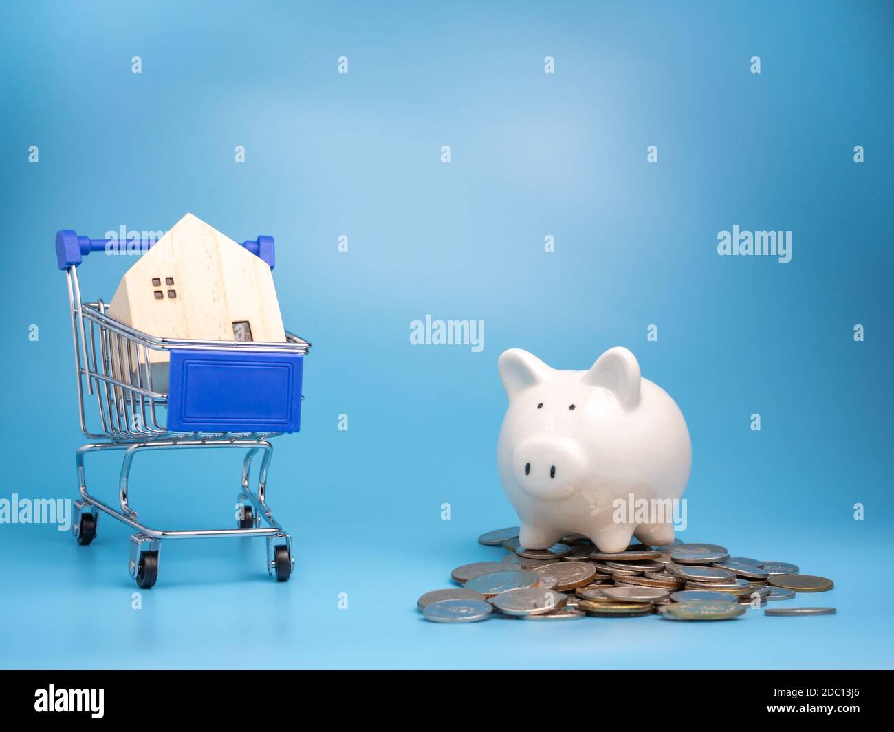 Ein Modell Holzhaus auf einem Warenkorb mit einem Haufen Münzen und Sparschwein auf blauem Hintergrund. Hypothekenkonzept. Geld und Haus. Finanzstatus Stockfoto