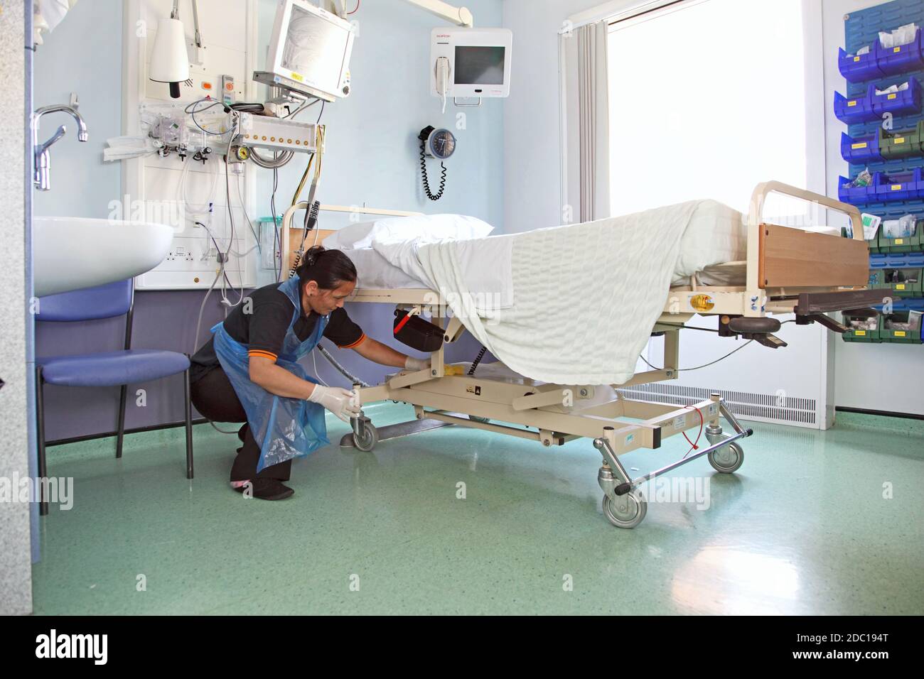 Ein Krankenhausreiniger wischt den Rahmen eines Bettes in einer modernen britischen Krankenstation ab. Stockfoto