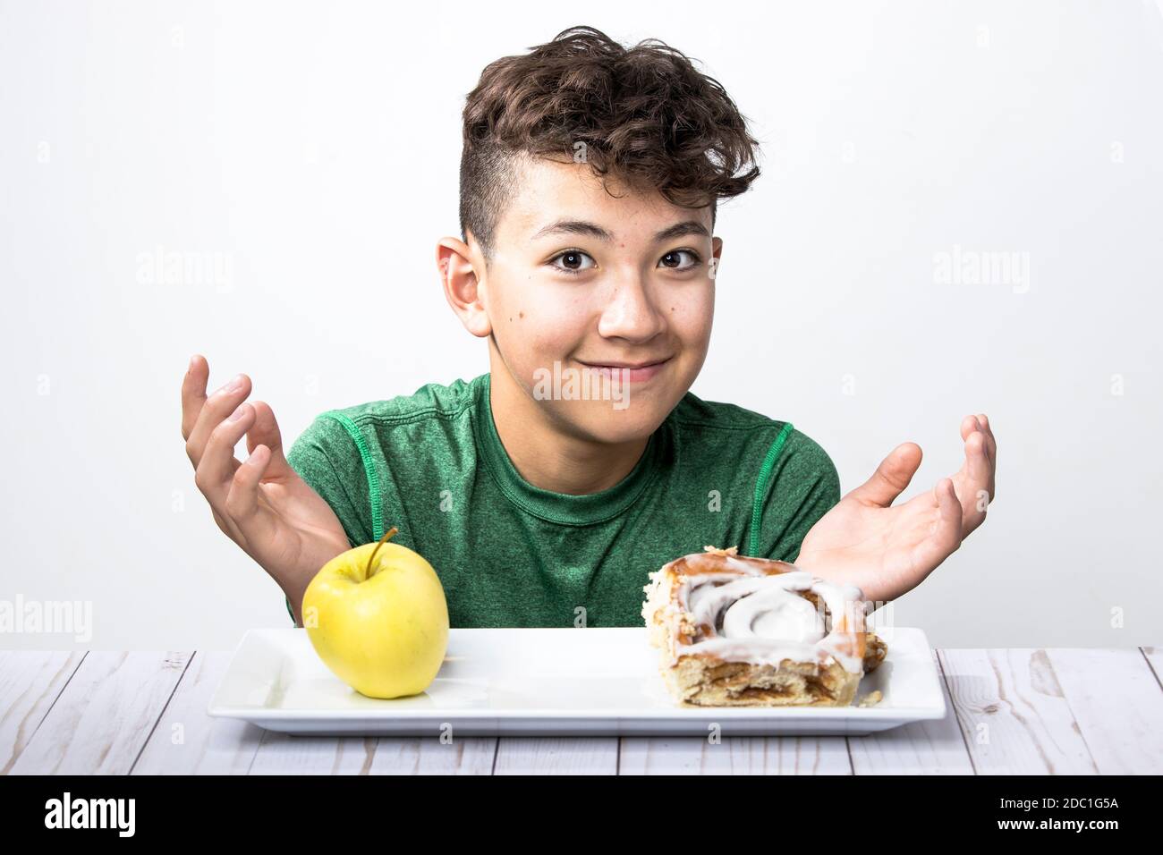 Ein Konzeptfoto eines Teenagers, der versucht, sich zwischen einem gesunden Apfel und einer süßen Zimtrolle zu entscheiden. Stockfoto