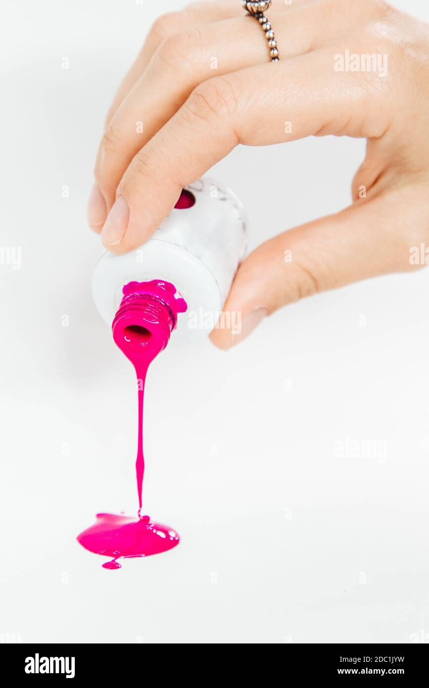 Gelpolitur wird über einen weißen Hintergrund gegossen. Die Hand hält ein Glas von leuchtend rosa Farbe Gel Politur. Stockfoto